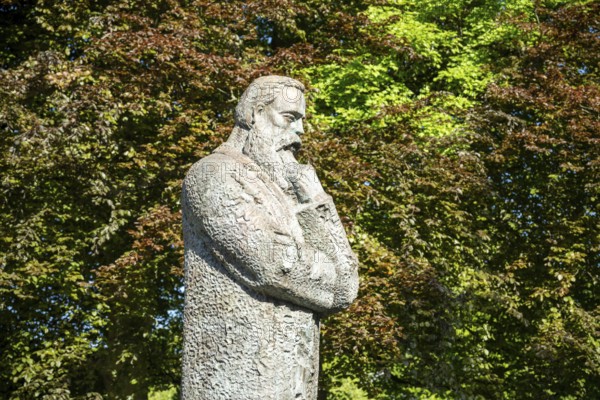 Stone statue of a pensive man surrounded by lush green trees in a park, statue of Friedrich Engels by sculptor Zeng Chenggang in the Engelsgarten Wuppertal Barmen