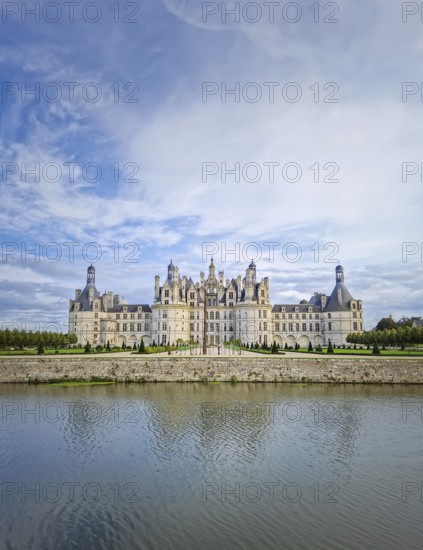 The symmetrical Château de Chambord is reflected in the still water, highlighting its magnificent Renaissance architecture with numerous turrets. The majestic castle stands beneath a beautiful sky