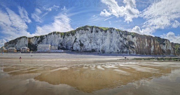 Panoramic view of Dieppe beach in Normandy, France. Majestic white chalk cliffs rise above a pebble shore, with the low tide revealing a vast expanse of wet sand reflecting the blue sky