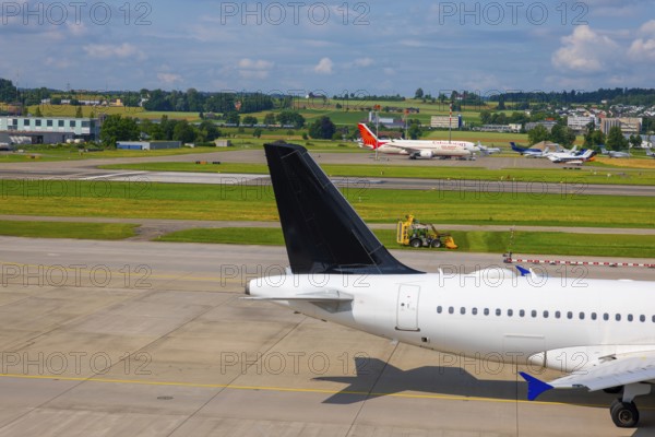 Passenger Airplane Taxiing on Runway and a Tractor Cutting the Grass in a Sunny Summer Day From the Airport in Kloten, Zurich, Zurich Canton, Switzerland