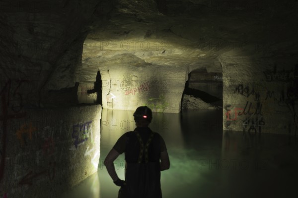 Person exploring illuminated, water-filled mine with graffiti, Ofenkaulen, Lost Place, Königswinter, North Rhine-Westphalia, Germany