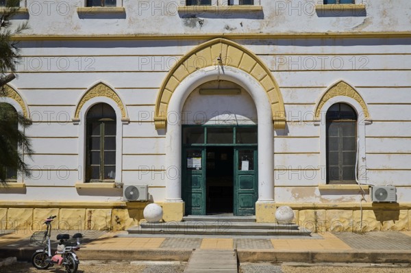 Historic building with arched entrance and small windows, bicycle in front, Historicism, Art Deco, Rationalism, Portolago, Lakki, Leros, Dodecanese, Greek Islands, Greece