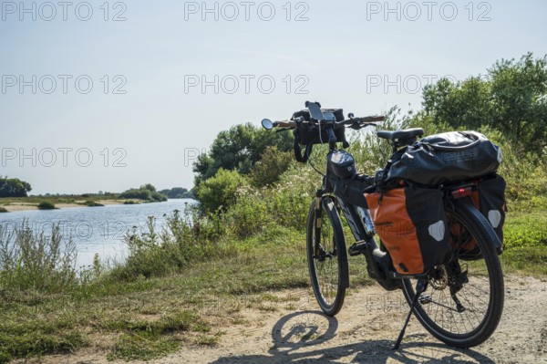 A bike with panniers stands on a sunny riverbank, embedded in nature, Weser cycle path, Weser, touring bike