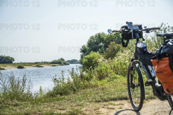 A bicycle stands on the riverbank, surrounded by a green landscape under a clear sky, Weser cycle path, Weser, touring bike