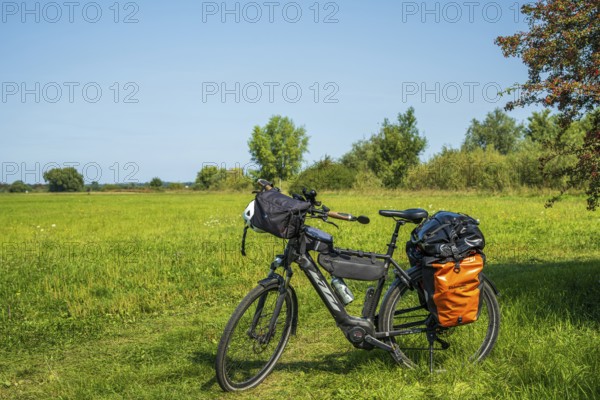 A bicycle stands on a green meadow under a blue sky, accompanied by light shadows of nature, Weser cycle path, Weser, touring bike