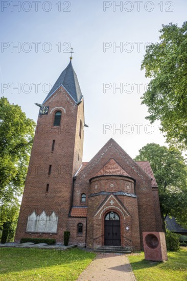 Brick church with Gothic tower and clock, surrounded by green trees under a blue sky, Weser cycle path, Kreuzkirche Schweringen, Schweringen Nienburg Weser, Lower Saxony