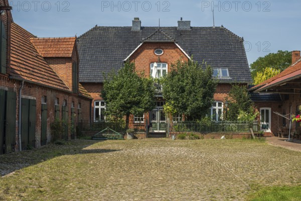 An idyllic brick farmhouse with trees and a cobbled courtyard under a sunny sky, Oiste, Blender, Lower Saxony, Germany