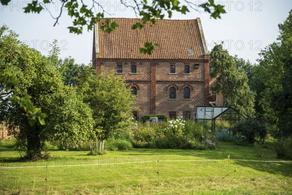 A large brick building with garden, surrounded by trees and vegetation on a summer's day, Bücken, district of Nienburg Weser, Lower Saxony