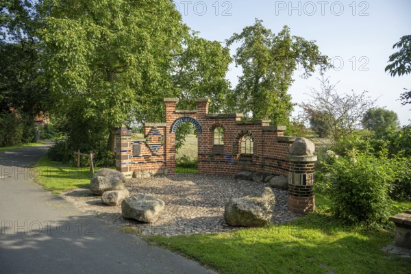 Brick wall with archway in a sunny park next to a path and trees, Bücken, district of Nienburg Weser, Lower Saxony