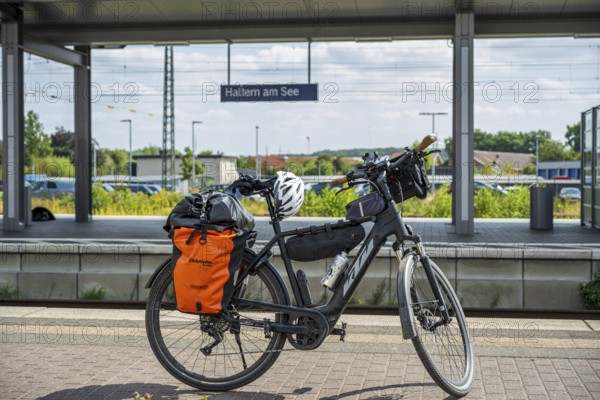 A bicycle with panniers stands at Haltern am See station, surrounded by summery nature and railway tracks, Haltern am See station, Münsterland, North Rhine-Westphalia, Germany