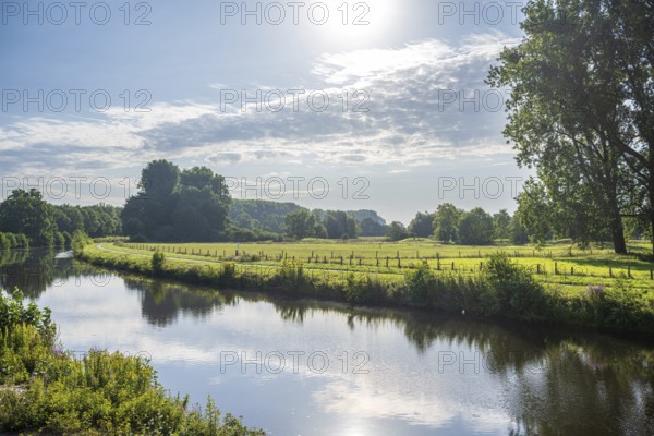 Sunny day by a river, green meadow and trees in the distance under a bright sky, Ems near Warendorf, Münsterland