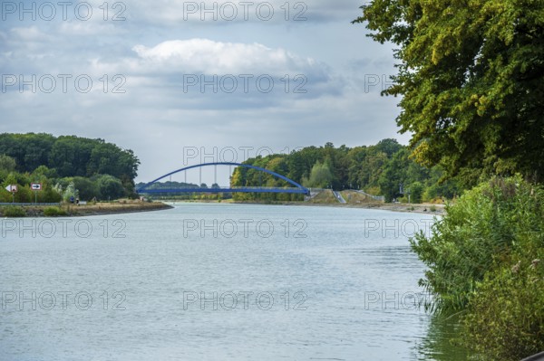 View of a canal with a modern blue bridge under a cloudy sky, surrounded by green trees, Senden, Münsterland, North Rhine-Westphalia, Germany