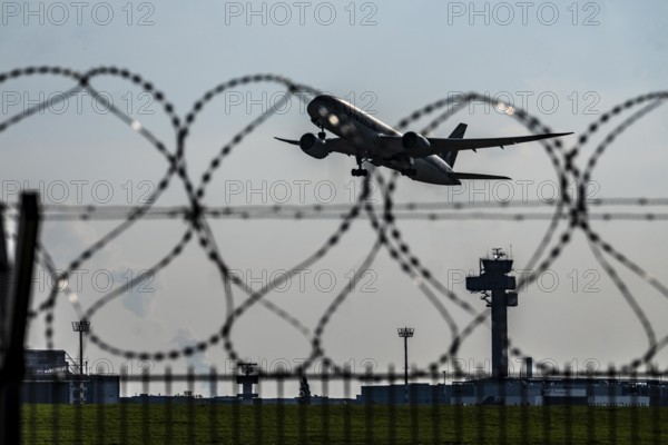 Symbolic image security at the airport, outer fence at Düsseldorf International Airport, steel wire fence, with S-wire rolls, NATO wire, on the top of the fence, aircraft taking off, air traffic control tower, DFS, North Rhine-Westphalia, Germany