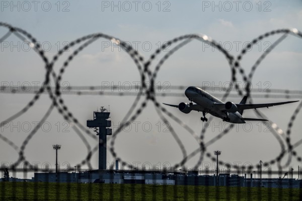 Symbolic image security at the airport, outer fence at Düsseldorf International Airport, steel wire fence, with S-wire rolls, NATO wire, on the top of the fence, aircraft taking off, air traffic control tower, DFS, North Rhine-Westphalia, Germany