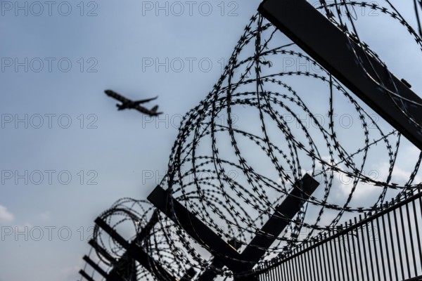 Symbolic image security at the airport, outer fence at Düsseldorf International Airport, steel wire fence, with S-wire rolls, NATO wire, on the top of the fence, aeroplane taking off, North Rhine-Westphalia, Germany