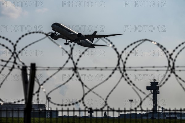 Symbolic image security at the airport, outer fence at Düsseldorf International Airport, steel wire fence, with S-wire rolls, NATO wire, on the top of the fence, aircraft taking off, air traffic control tower, DFS, North Rhine-Westphalia, Germany