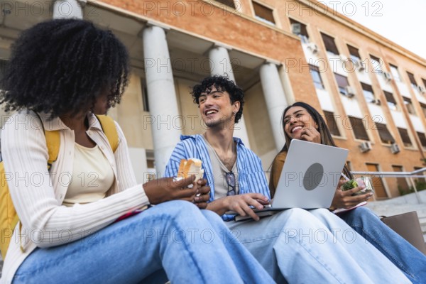 Group of happy young multiracial students sitting on steps outside a university building, enjoying a casual lunch and socializing between classes on campus