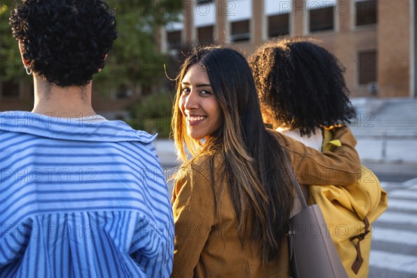 Diverse young adult students walking on a university campus during the day, one female student turning back and smiling, depicting friendship, education, and college life