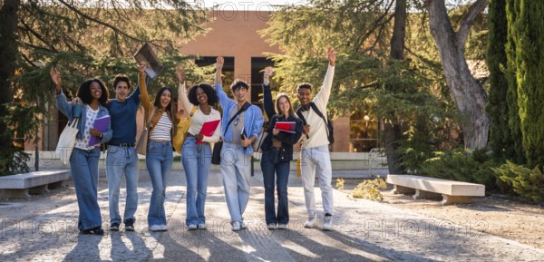 Group of young, happy, diverse university students standing together, raising their hands in celebration of academic success and friendship on college campus
