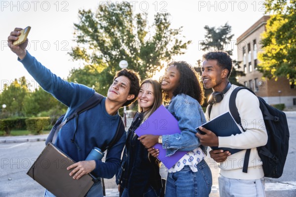 Diverse group of smiling university students recording a selfie outdoors on campus, holding books and backpacks, representing friendship, education, and youth