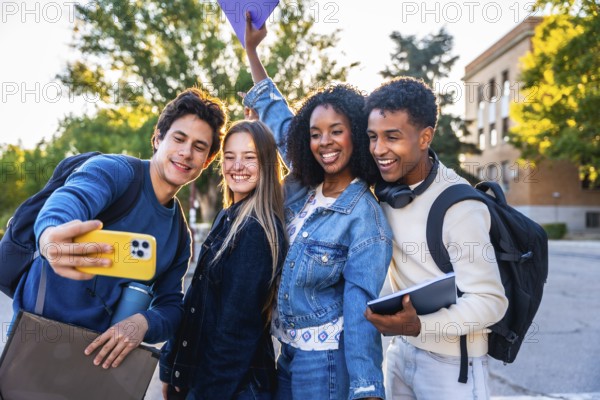 Happy diverse university friends smiling and taking a campus selfie with a smartphone, enjoying friendship, studying together outdoors and sharing moments of student life and connection