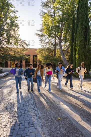 Group of diverse university students hurrying with textbooks and backpacks on a cobblestone path, expressing joy and energy under morning sunlight on campus