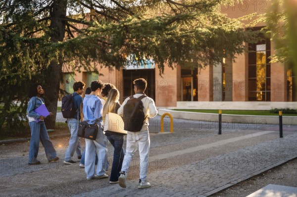 Group of diverse university students with backpacks and folders walking together on campus, heading towards a modern educational building during a sunny day
