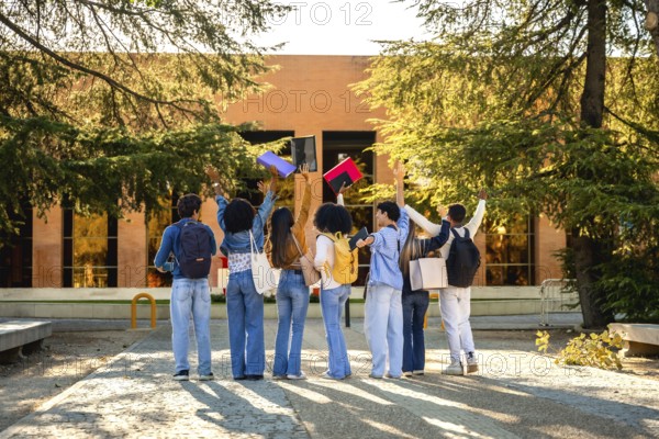 Diverse students seen from behind on a sunlit campus path throwing colorful notebooks into the air in celebration of academic success, friendship and a bright future