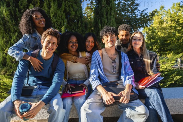 Diverse group of happy young male and female university students sitting outdoors on campus, embracing friendship, education, and multicultural connections while looking at camera