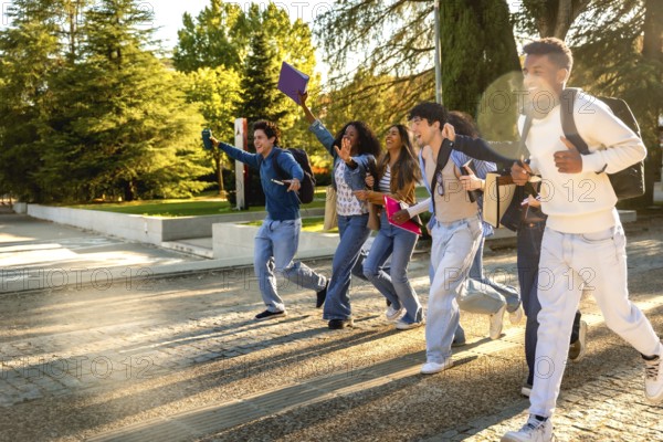Group of excited multiracial students. Wearing casual clothes and carrying backpacks and books. Running across a university campus with trees in the background. Celebrating success or rushing to class