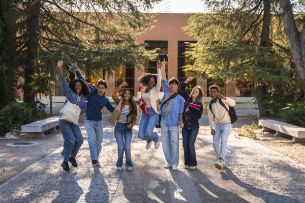 Group of excited multi ethnic students celebrating success and friendship, walking and jumping on a college campus with books and backpacks under the warm sunlight