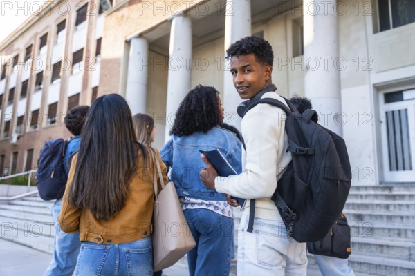 Group of diverse young university students with backpacks and books walking up the steps towards a campus building, representing education, friendship, and student life