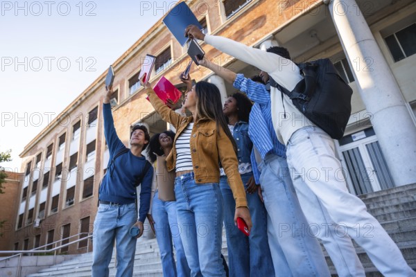 Group of happy young university students raising books and smartphones in the air, celebrating academic success and friendship on graduation day or end of exams at college campus