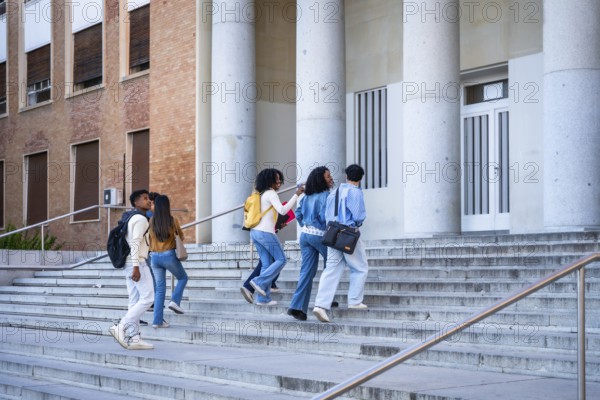 Diverse group of college students walking up wide outdoor steps toward a university building with large columns, backpacks and books, heading to class or campus event