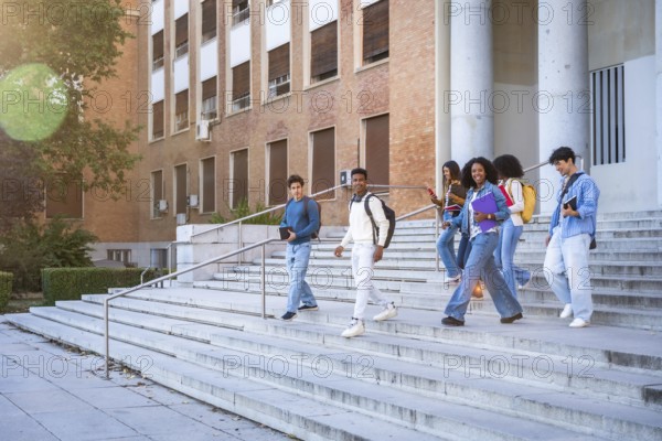 Diverse group of young students smiling, talking, and walking down the outdoors stairs of a university building, carrying books and backpacks, representing education and college life