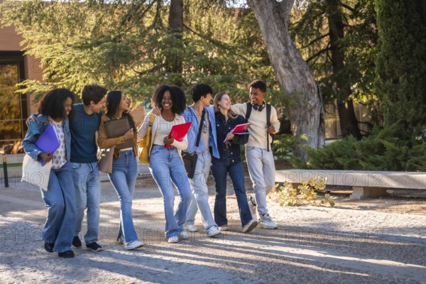 Group of multicultural university students walking and talking cheerfully together, carrying books, a backpack, and folders while enjoying their time on campus after class