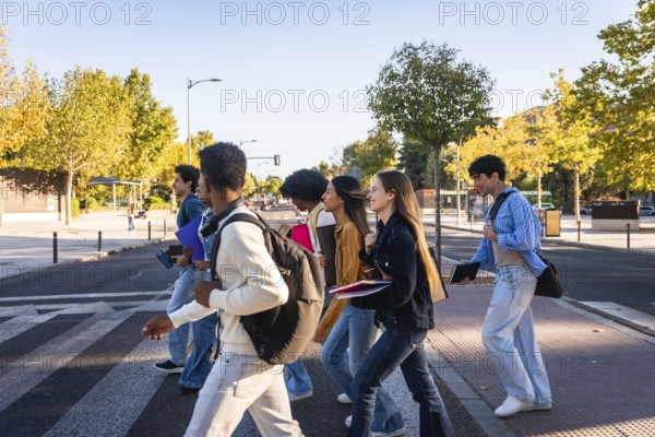 Group of diverse university students with backpacks and books walking across a pedestrian crosswalk, smiling and talking, representing education, friendship, and student life on a sunny day