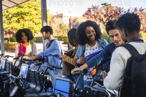 Group of happy diverse university students activating a shared bicycle from a station, preparing to ride on campus, representing sustainable urban transport