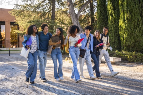 Diverse group of happy young university students walking together on campus, carrying books and binders, representing friendship, education, and collaboration