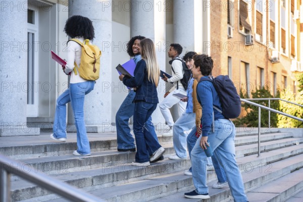 Diverse group of college students walking up campus stairs with backpacks and books, enjoying sunny day, teamwork and ambition as they head toward higher education and future success