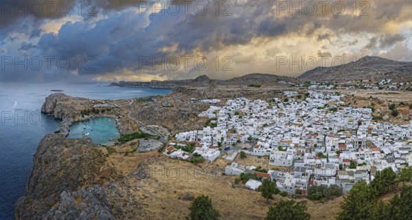 Atmospheric view of the coastal town of Lindos under a dramatic sky at dusk, Acropolis, Lindos, Rhodes, island, Greece