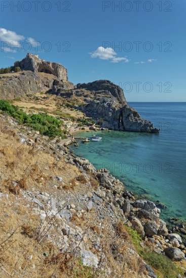 Steep cliffs Paulus Bay of Lindos over crystal clear blue water under a bright blue sky, Acropolis, Lindos, Rhodes, Island, Greece