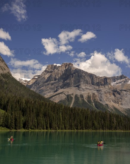 People canoeing on Emerald Lake, bordered by trees and the Canadian Rocky Mountains under a clear sky within Yoho National Park in Alberta, Canada, North Canada