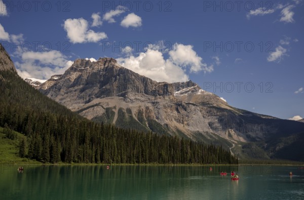 Canoes navigating Emerald Lake surrounded by towering Canadian Rocky Mountains under a clear blue sky within Yoho National Park in Alberta, Canada, North Canada