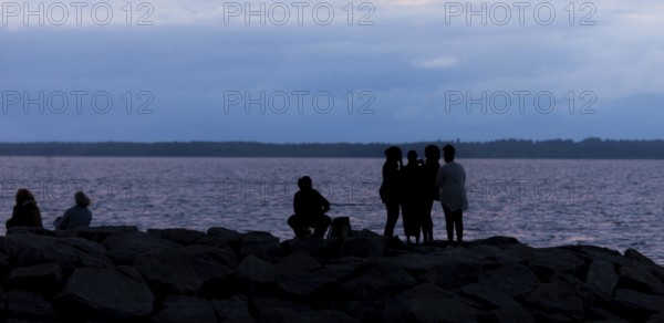 Group of silhouetted figures by a municipal lake at dusk in Ottawa, Ontario, Canada, North America