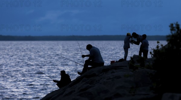 Silhouetted figures fishing and interacting by a lake at night in Ottawa, Ontario, Canada, North America
