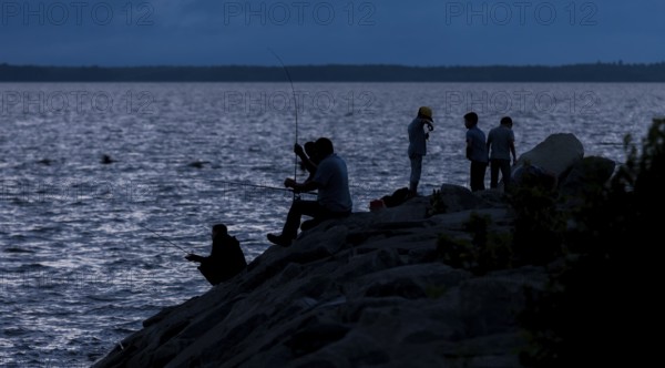 Group of people fishing at night, silhouetted against the water in Ottawa, Ontario, Canada, North America