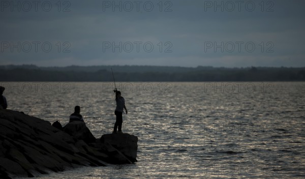 A person fishing on a rocky shore at dusk with a calm lake in Ottawa, Ontario, Canada, North America