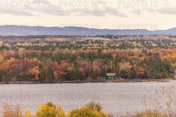 A small cabin nestled in an autumn forest along the Ottawa River with hills in the distance in Ottawa, Ontario, Canada, North America