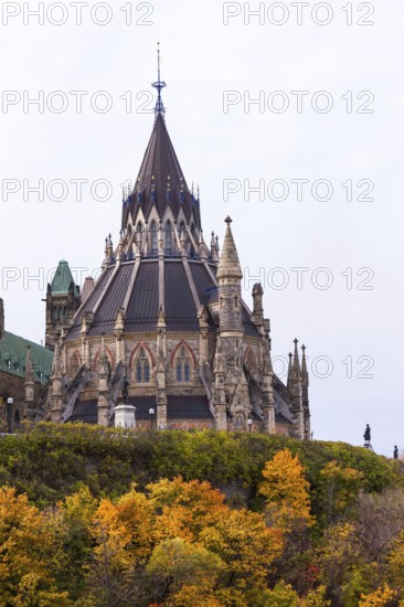 A Gothic-style Canadian Parliament building with a prominent spire, surrounded by colorful autumn foliage, highlighting historical elegance in Ottawa, Ontario, Canada, North America